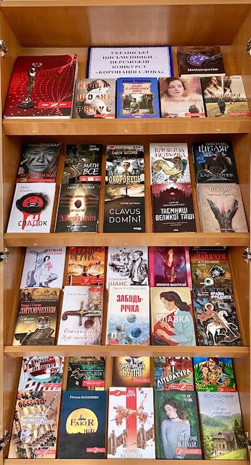 Книжкова виставка на полицях стелажа, де представлені твори сучасних українських авторів-переможців 'Коронації слова', зокрема Люко Дашвар, Василя Шкляра та братів Капранових