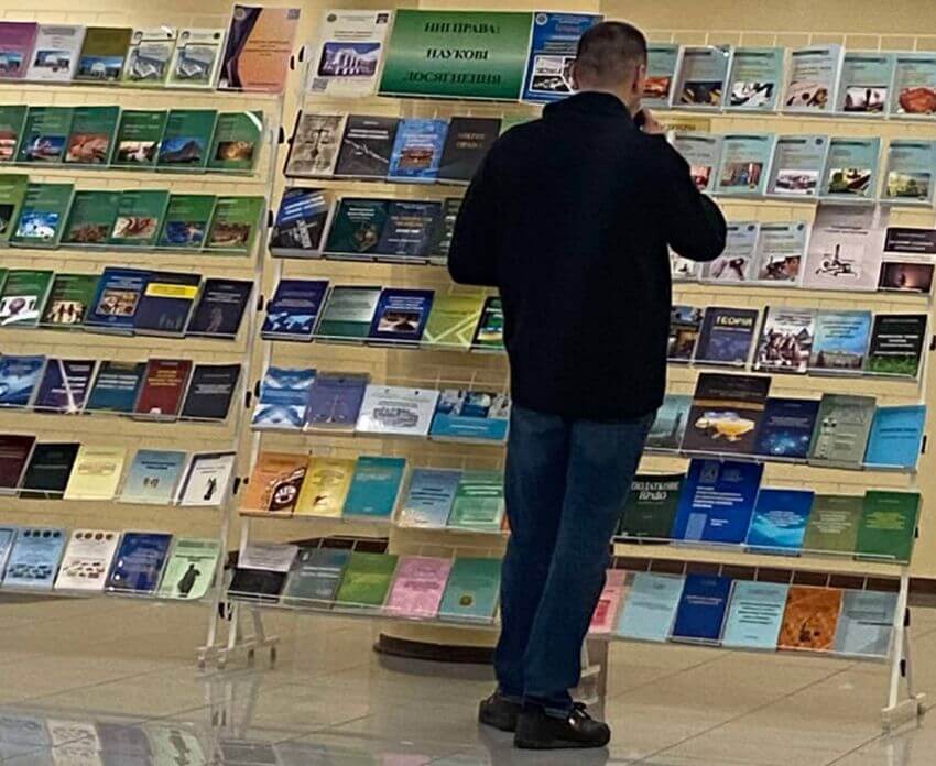 Чоловік розглядає виставку наукових праць та юридичної літератури, представлену на стелажах у холі університету